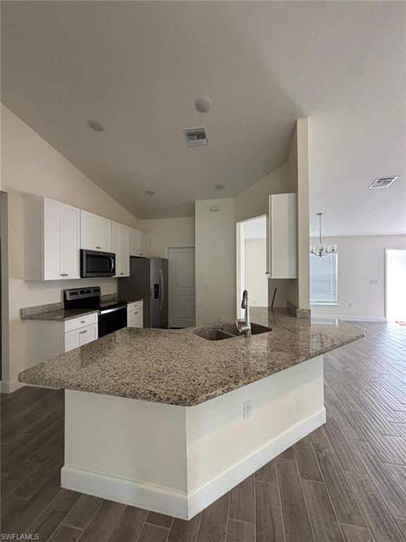 Kitchen with wood finish floors, white cabinetry, light stone countertops, appliances with stainless steel finishes, and a peninsula