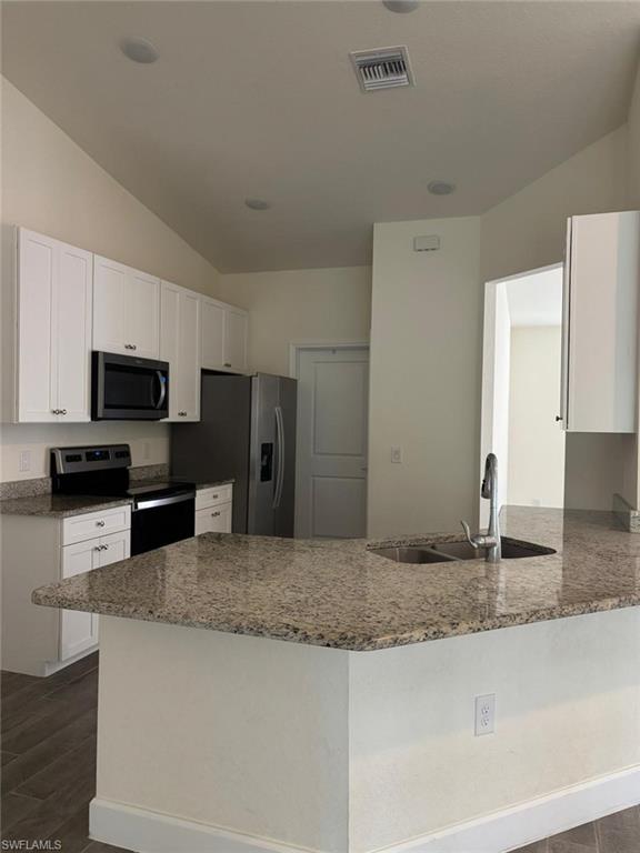 Kitchen featuring a peninsula, stainless steel appliances, dark stone counters, white cabinets, and lofted ceiling