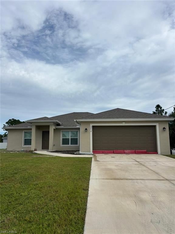View of front of house with stucco siding, driveway, a front yard, and a shingled roof