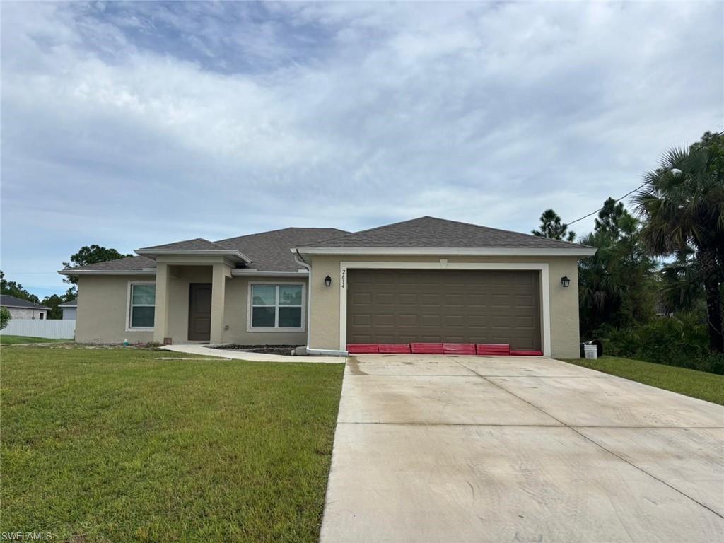 View of front of property with stucco siding, driveway, a front yard, a shingled roof, and a garage