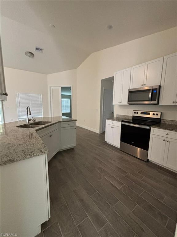 Kitchen featuring appliances with stainless steel finishes, dark stone counters, white cabinetry, dark wood-style flooring, and lofted ceiling
