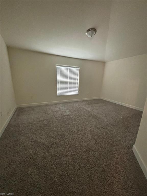 Unfurnished room featuring dark carpet and lofted ceiling