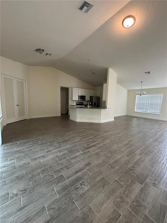 Unfurnished living room featuring vaulted ceiling, wood finish floors, and a textured ceiling