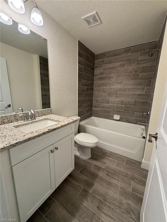 Bathroom featuring shower / bath combination, wood finish floors, vanity, a textured ceiling, and a textured wall