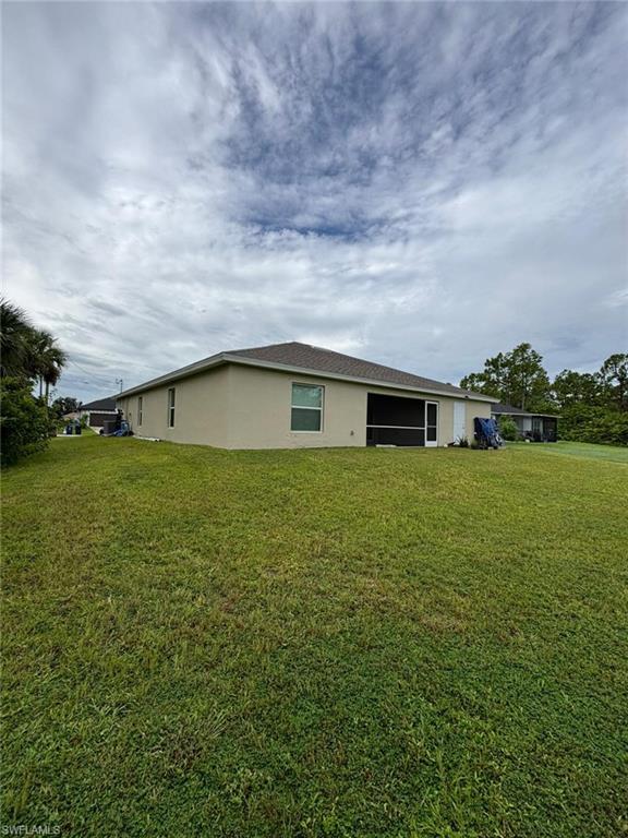 Rear view of property featuring a lawn, stucco siding, and a sunroom