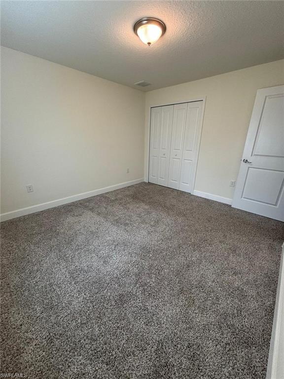 Unfurnished bedroom with carpet, a textured ceiling, and a closet