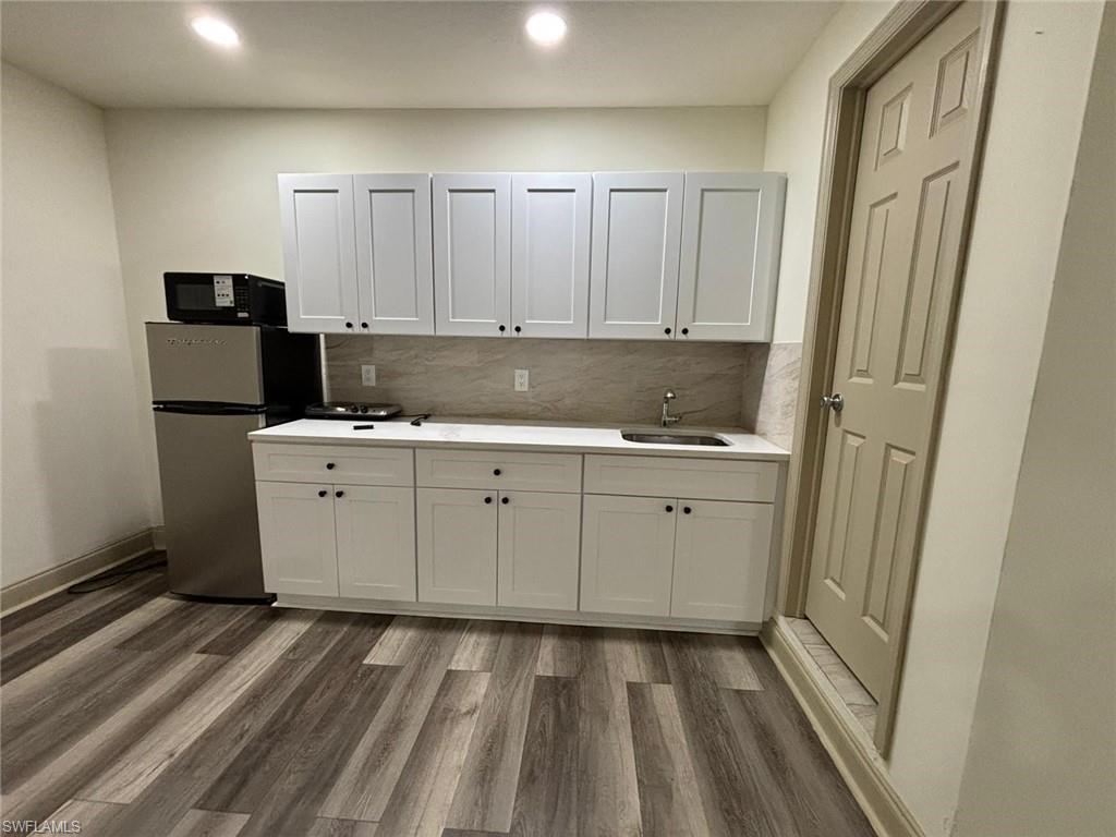 Kitchen with dark wood-style flooring, freestanding refrigerator, white cabinets, decorative backsplash, and recessed lighting