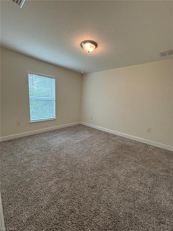 Carpeted empty room with a textured ceiling and baseboards