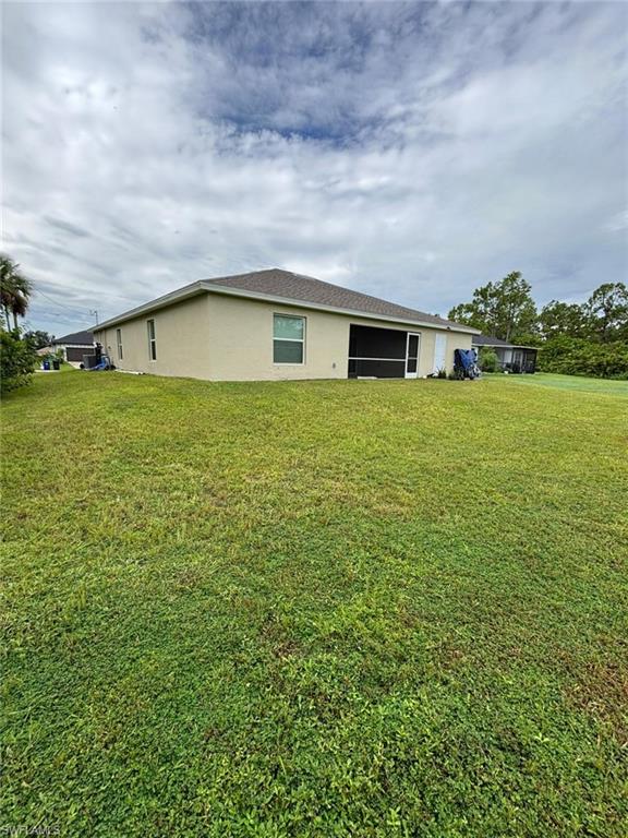 Rear view of property featuring a yard, stucco siding, and a sunroom