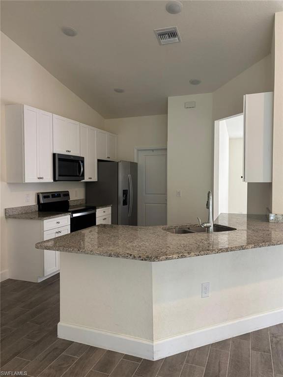 Kitchen featuring wood finish floors, a peninsula, stainless steel appliances, white cabinets, and dark stone counters