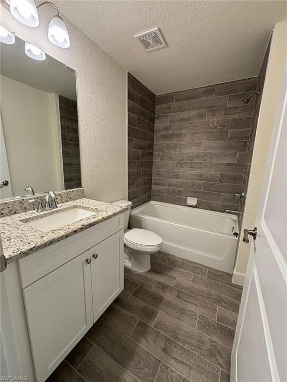 Bathroom with wood finish floors, shower / tub combination, vanity, a textured ceiling, and a textured wall