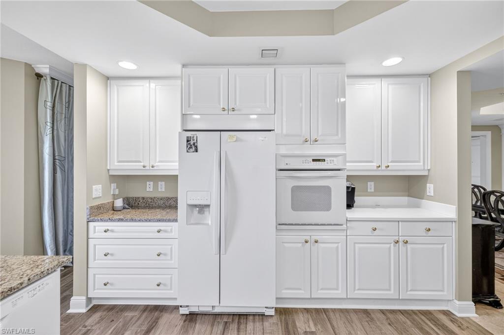 Kitchen with white appliances, white cabinetry, recessed lighting, light wood-style flooring, and a raised ceiling