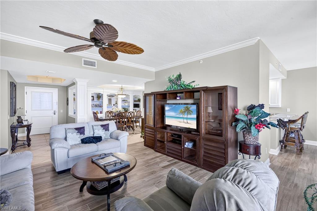 Living room with crown molding, wood finished floors, decorative columns, and a ceiling fan