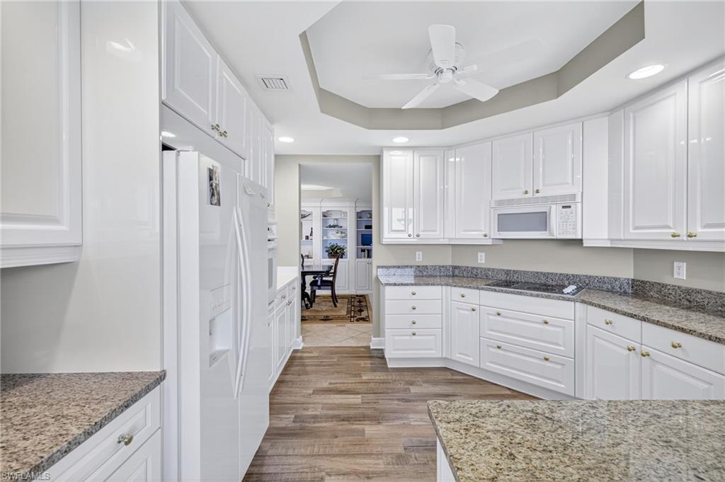Kitchen featuring a raised ceiling, white cabinetry, white appliances, light stone countertops, and recessed lighting