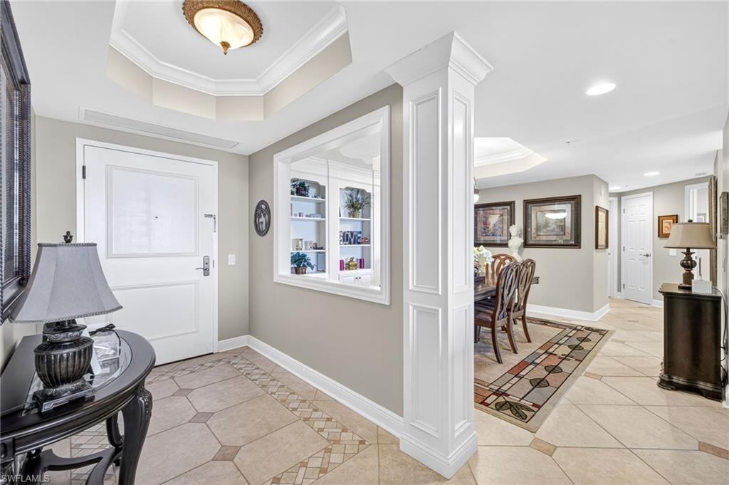 Entryway featuring a tray ceiling, light tile patterned floors, ornamental molding, recessed lighting, and decorative columns