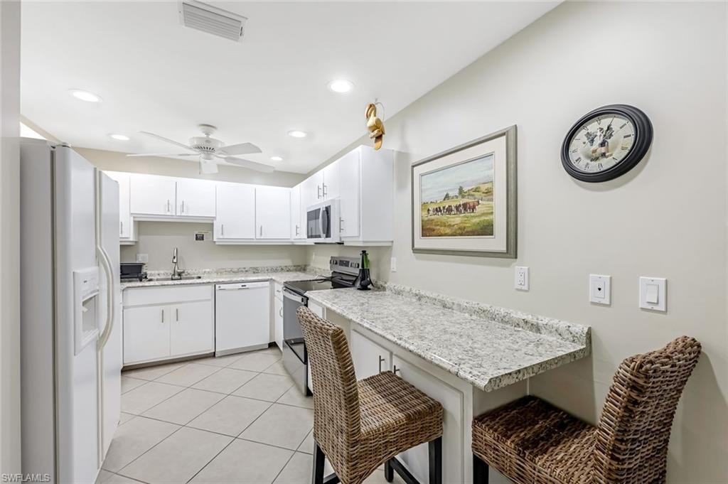 Kitchen featuring white appliances, white cabinets, a kitchen breakfast bar, light tile patterned flooring, and recessed lighting