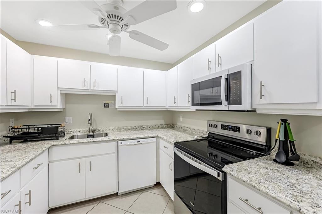 Kitchen with white appliances, white cabinets, light tile patterned flooring, light stone counters, and ceiling fan