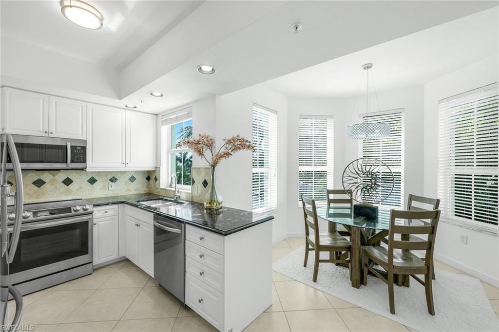 Kitchen with dark stone counters, recessed lighting, stainless steel appliances, light tile patterned floors, and white cabinets