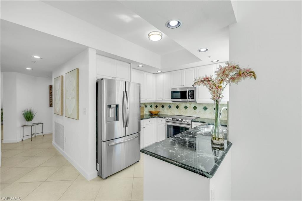 Kitchen with stainless steel appliances, tasteful backsplash, white cabinets, light tile patterned floors, and recessed lighting