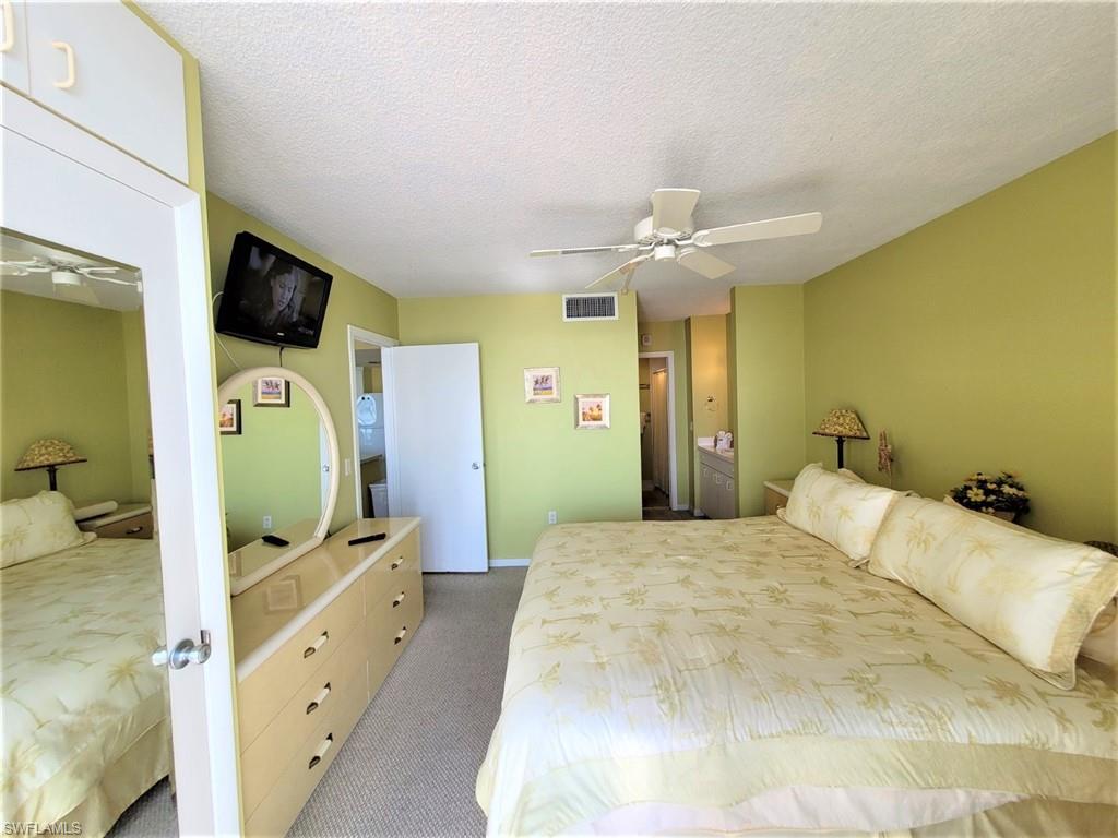 Bedroom with a textured ceiling, light colored carpet, connected bathroom, ceiling fan, and a closet