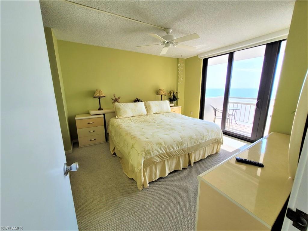 Carpeted bedroom featuring a textured ceiling, expansive windows, access to exterior, a water view, and ceiling fan