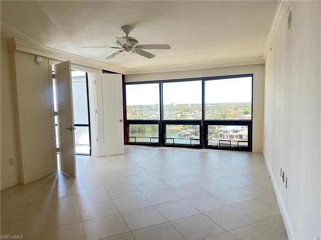 Empty room with ornamental molding, light tile patterned flooring, and ceiling fan