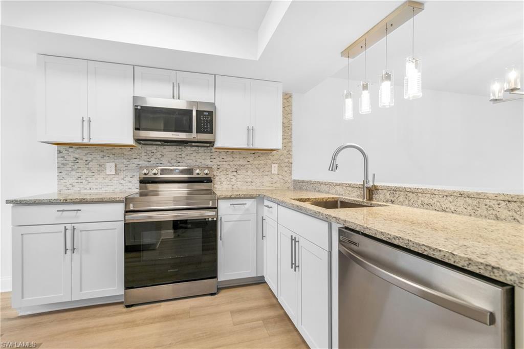 Kitchen featuring stainless steel appliances, backsplash, white cabinets, hanging light fixtures, and light stone counters