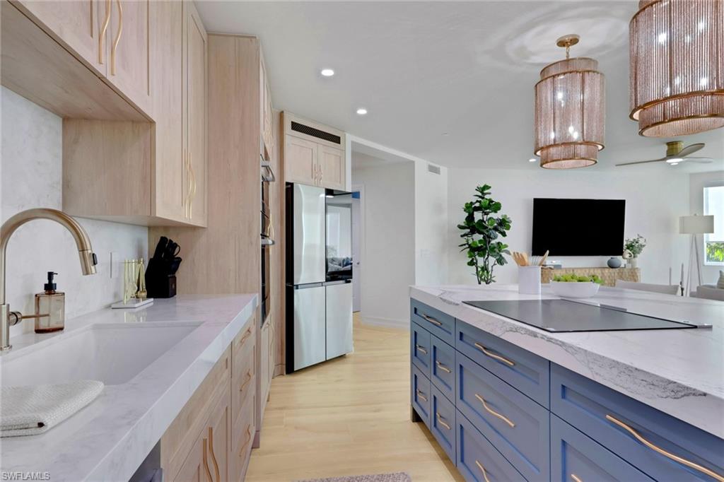 Kitchen with blue cabinets, light stone counters, recessed lighting, light wood finished floors, and hanging light fixtures