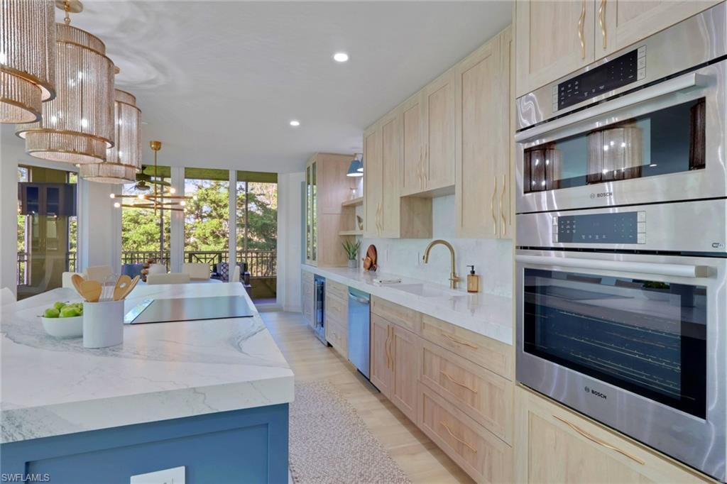 Kitchen featuring appliances with stainless steel finishes, light brown cabinetry, light stone counters, a chandelier, and decorative backsplash