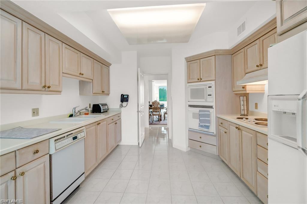 Kitchen with light brown cabinetry, white appliances, and light countertops