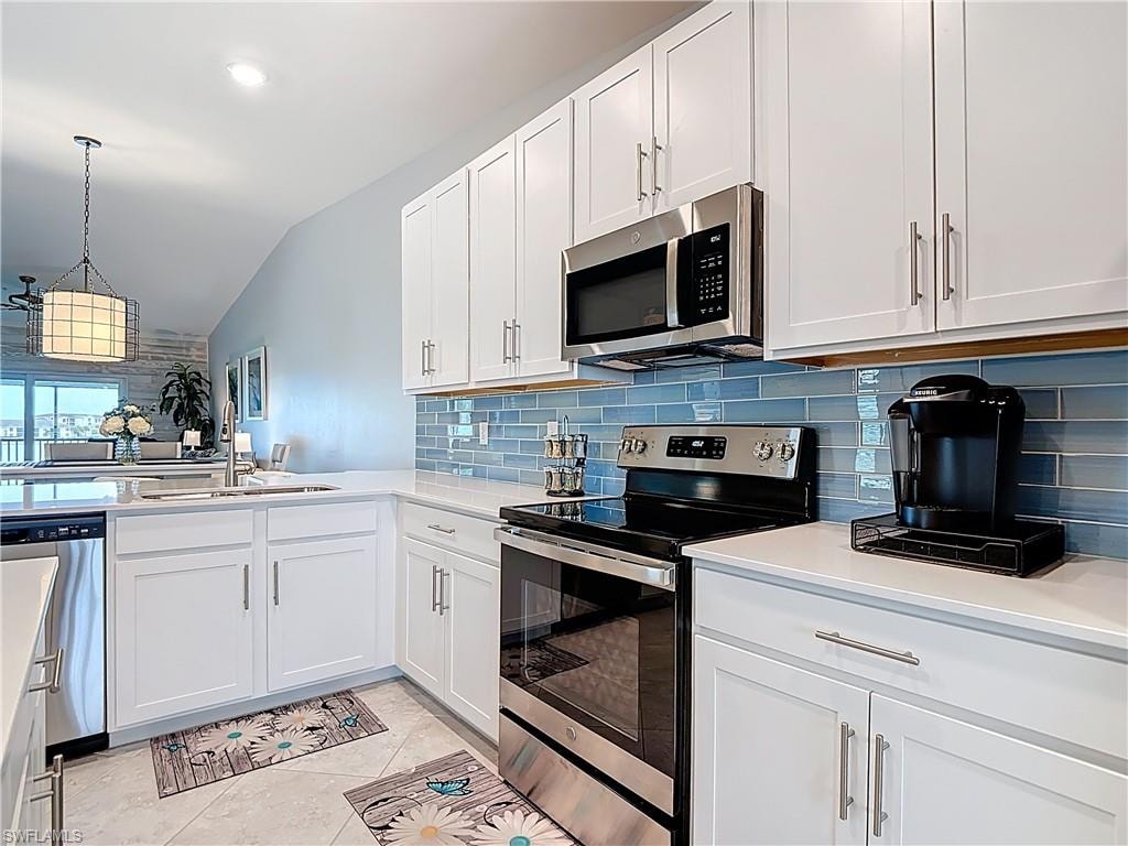 Kitchen featuring stainless steel appliances, white cabinetry, tasteful backsplash, lofted ceiling, and decorative light fixtures