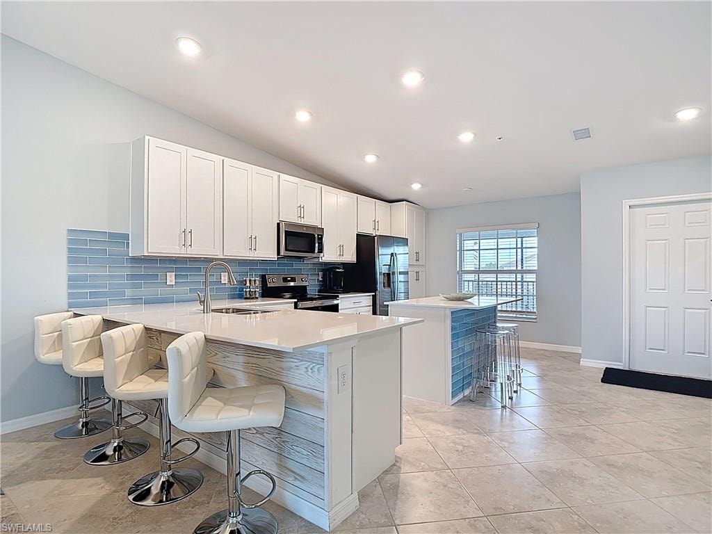 Kitchen with a kitchen bar, tasteful backsplash, white cabinetry, a center island, and a peninsula