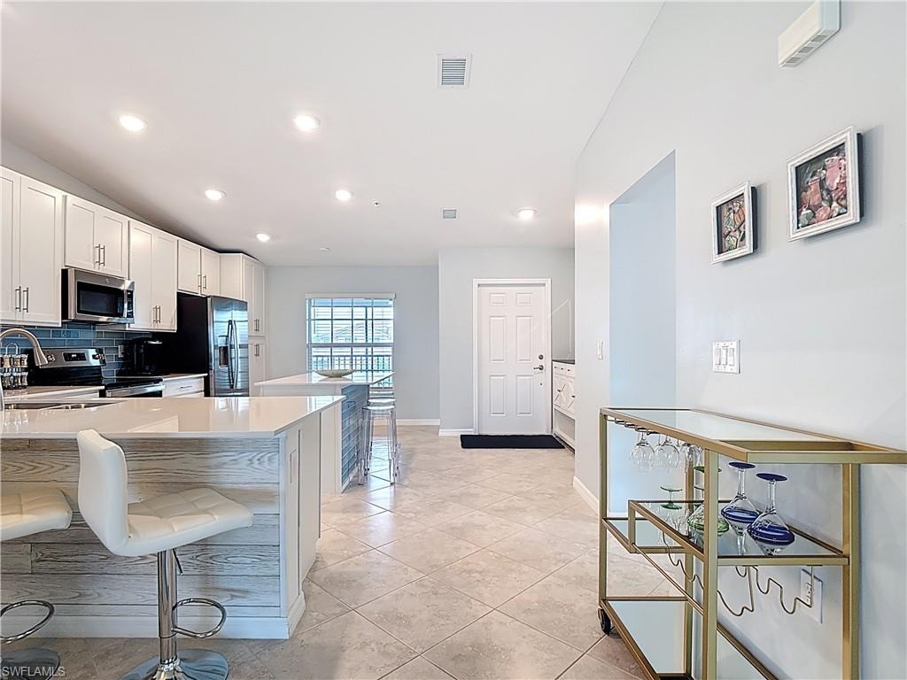 Kitchen featuring white cabinets, a breakfast bar area, tasteful backsplash, stainless steel appliances, and light stone countertops