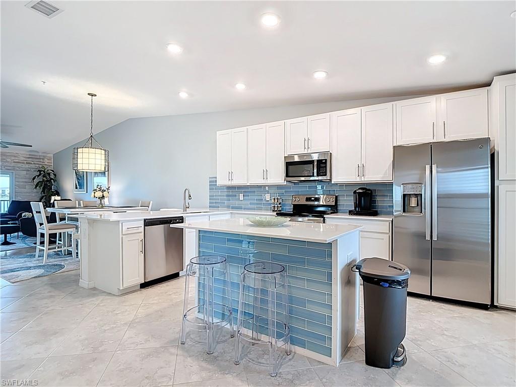 Kitchen with hanging light fixtures, white cabinets, backsplash, vaulted ceiling, and a kitchen bar