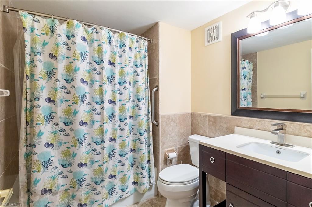Full bathroom featuring vanity, tile walls, a wainscoted wall, and shower / bath combo