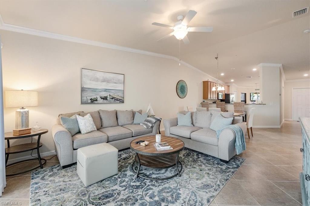 Tiled living room with ornamental molding, lofted ceiling, and ceiling fan