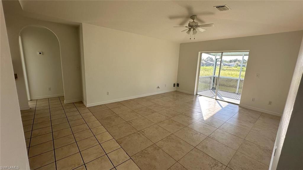 Empty room featuring arched walkways, light tile patterned floors, and ceiling fan