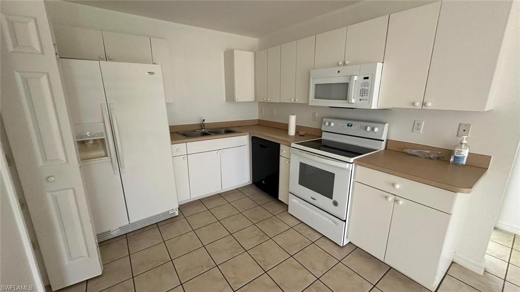 Kitchen featuring white appliances, white cabinetry, light tile patterned flooring, and light countertops