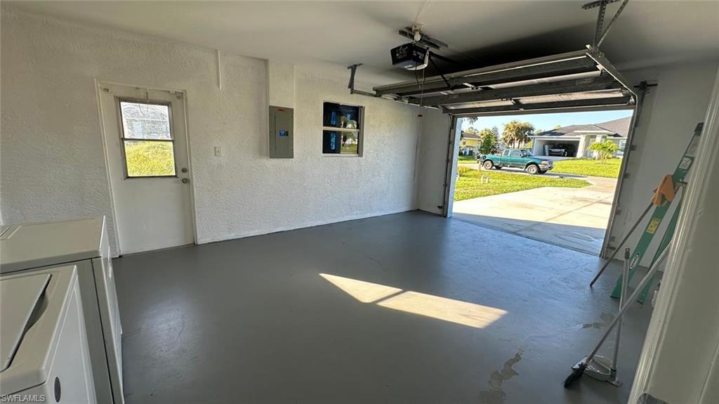 Garage featuring a textured wall, electric panel, independent washer and dryer, and a garage door opener
