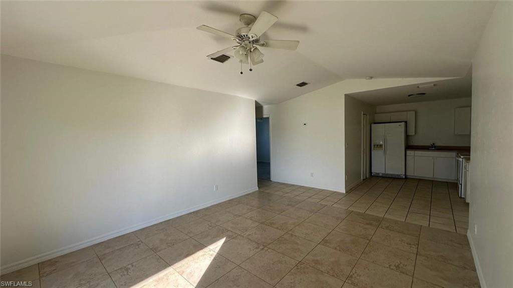 Empty room featuring ceiling fan, lofted ceiling, and light tile patterned flooring