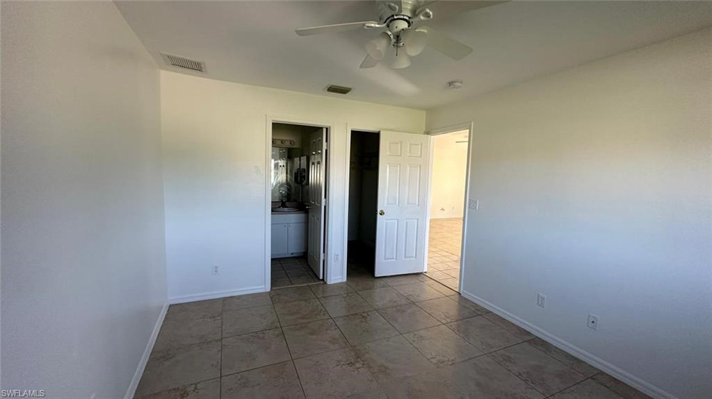 Unfurnished bedroom featuring a walk in closet, tile patterned floors, a ceiling fan, and ensuite bathroom