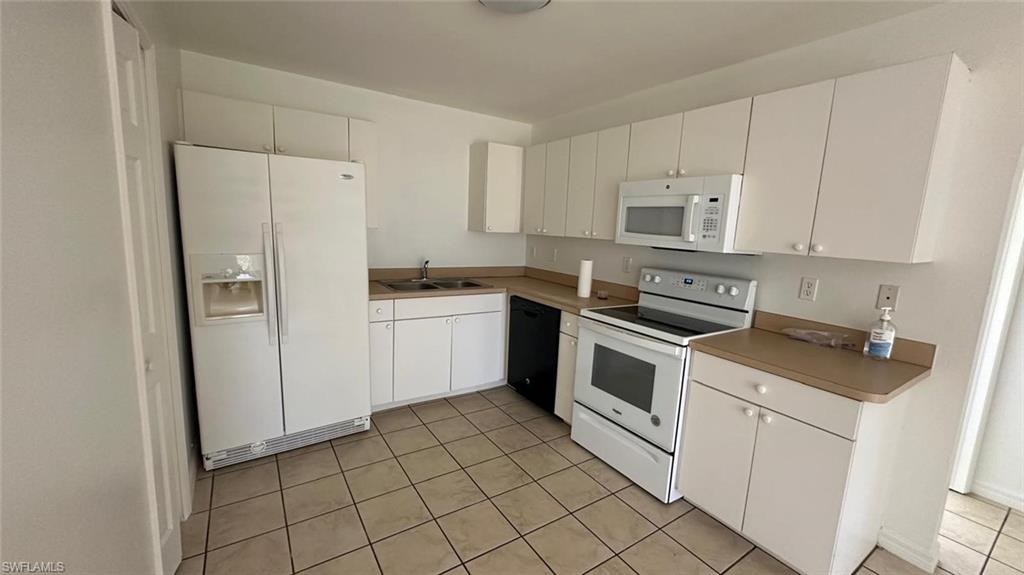 Kitchen featuring white appliances, white cabinets, light tile patterned floors, and light countertops
