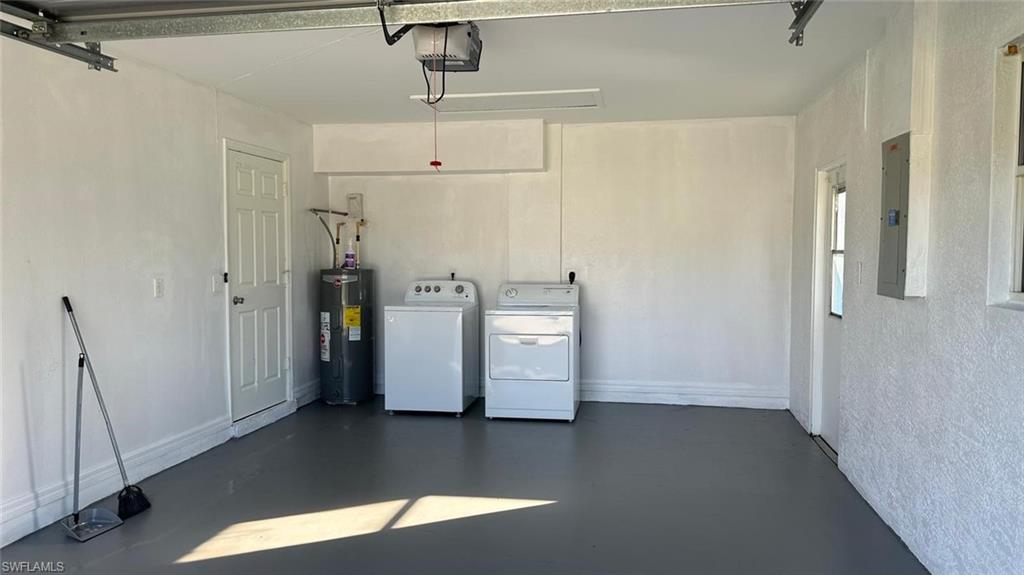 Garage featuring electric water heater, electric panel, washer and clothes dryer, and a garage door opener