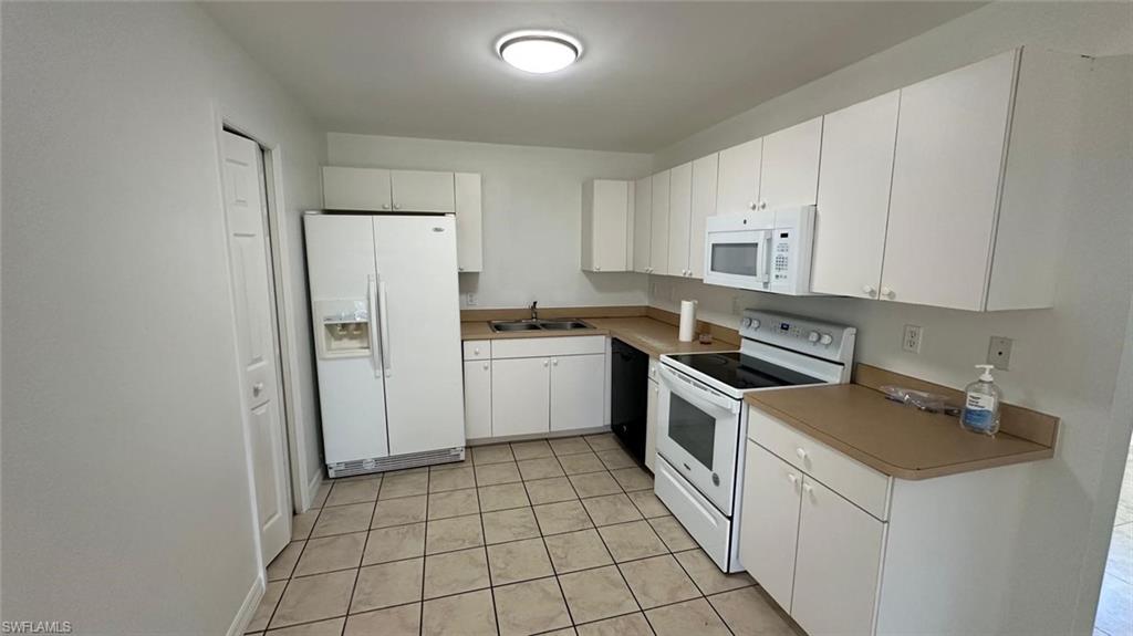 Kitchen featuring white appliances, white cabinetry, light tile patterned floors, and light countertops