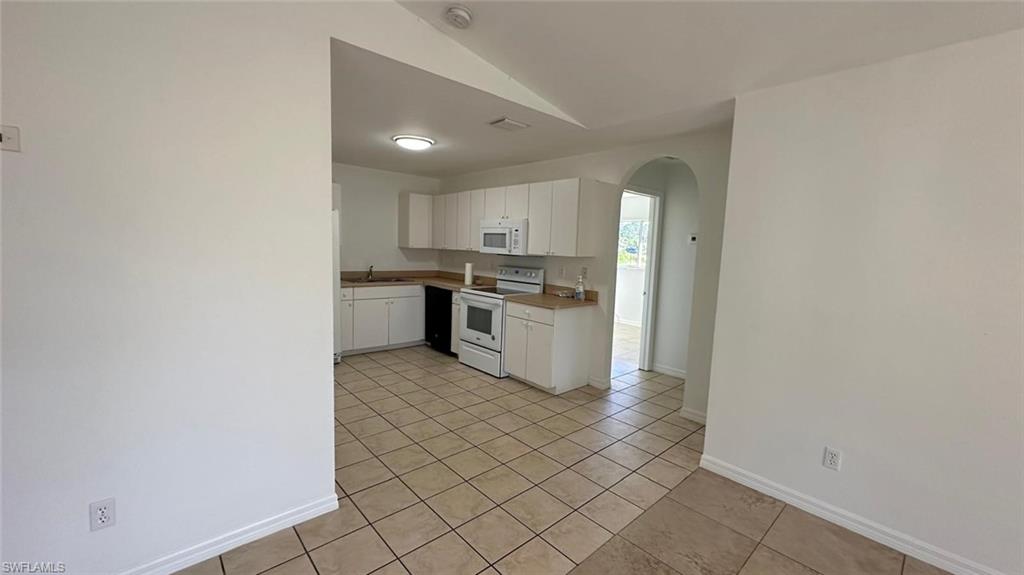 Kitchen featuring arched walkways, white appliances, white cabinetry, light tile patterned flooring, and vaulted ceiling
