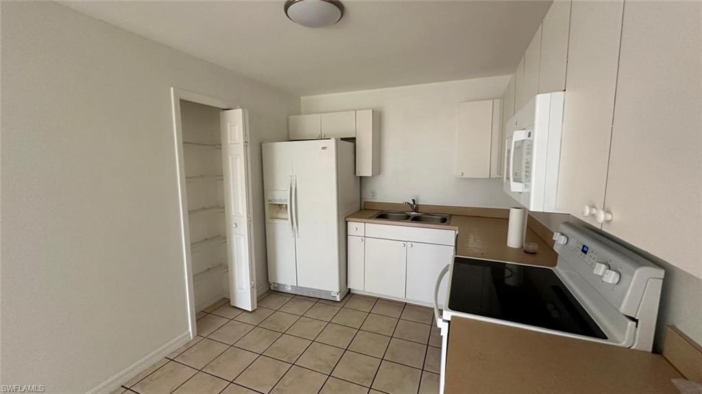 Kitchen featuring white appliances, white cabinets, light tile patterned floors, and light countertops