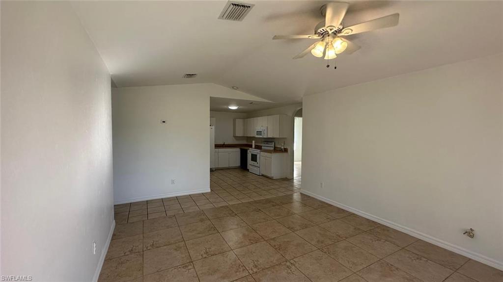 Unfurnished living room featuring lofted ceiling, arched walkways, light tile patterned floors, and ceiling fan