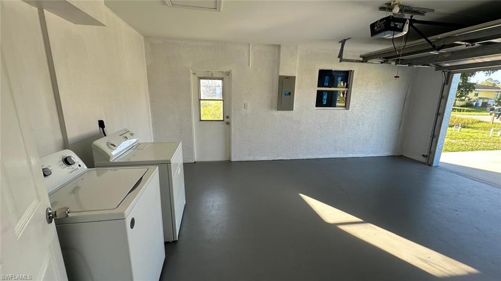 Laundry area with a textured wall, separate washer and dryer, electric panel, and a garage