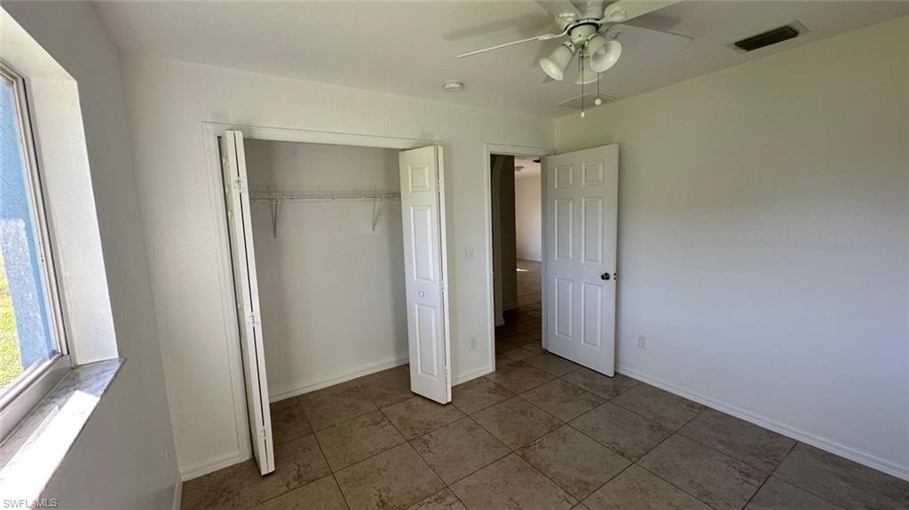 Unfurnished bedroom featuring a ceiling fan, a closet, multiple windows, and tile patterned floors