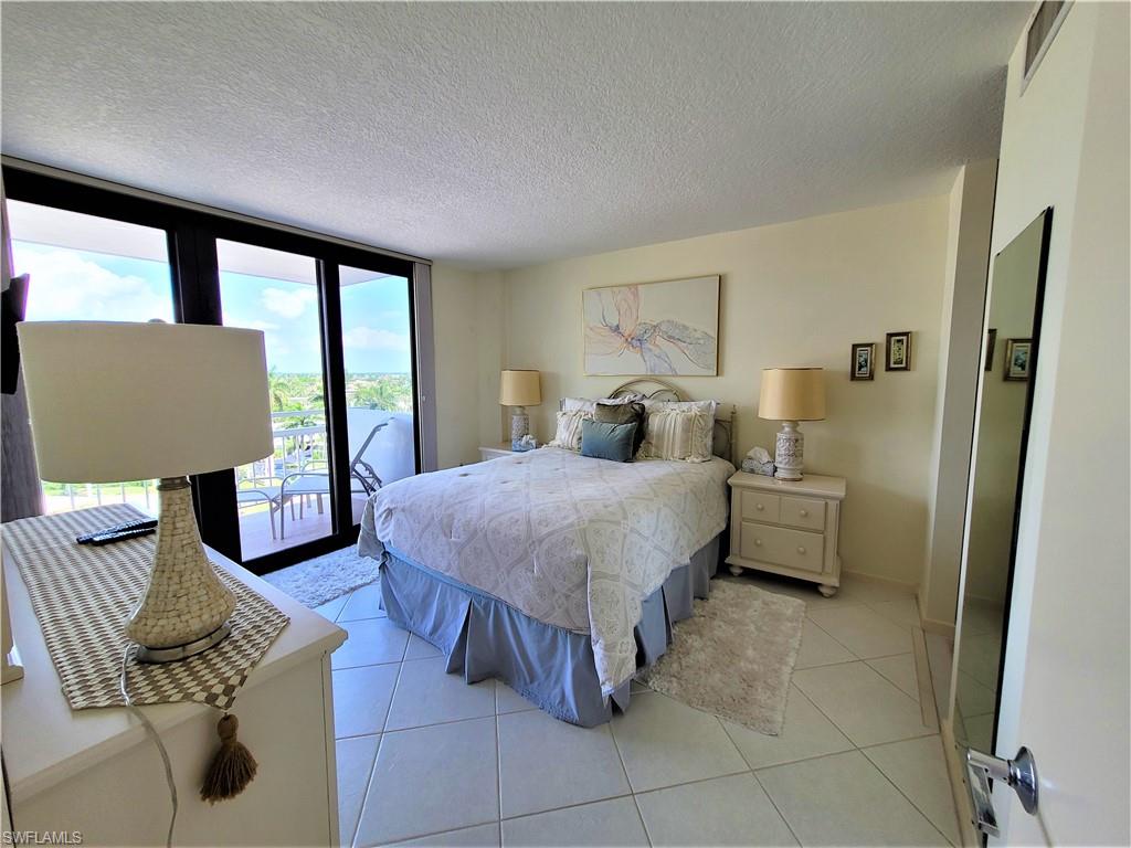 Bedroom with a textured ceiling, light tile patterned floors, a wall of windows, and access to outside